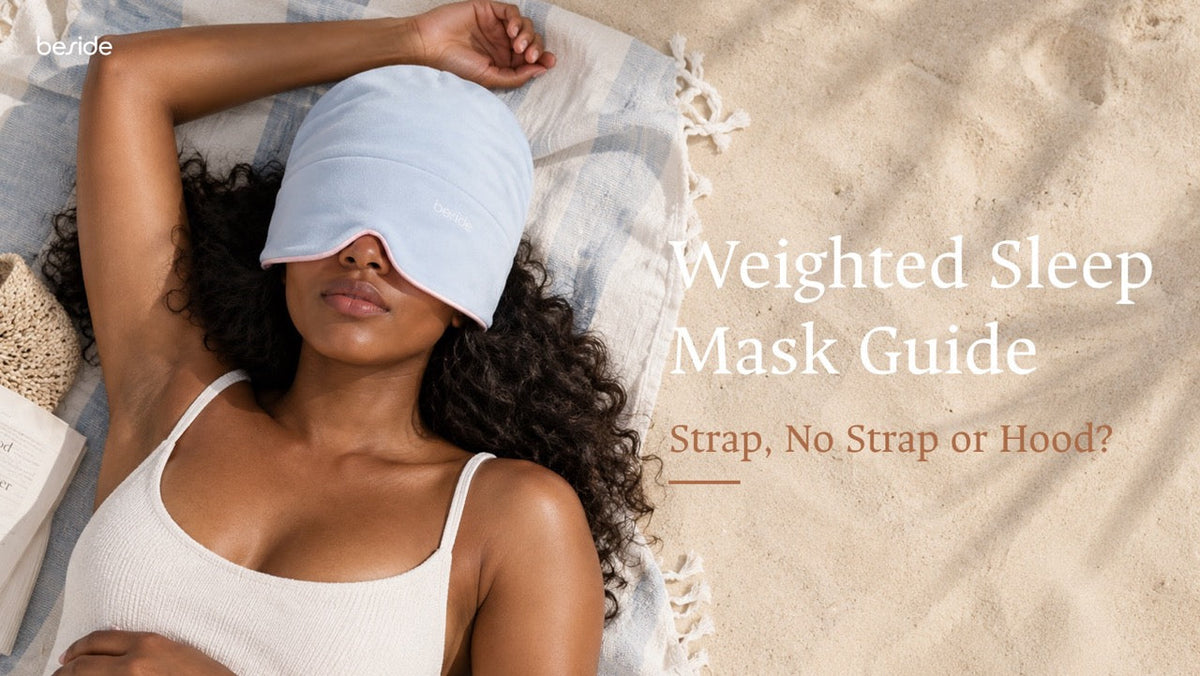 A woman lying on a sandy beach blanket wears a light blue weighted sleep hood, with overlaid text reading “Weighted Sleep Mask Guide: Strap, No Strap or Hood?”.