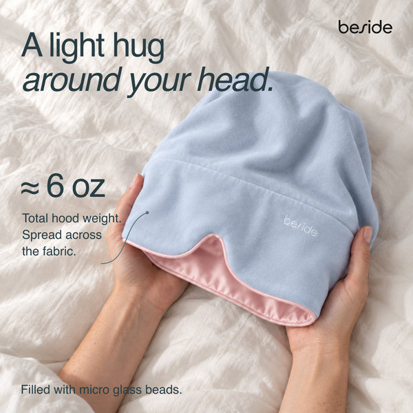 Hands holding open the Blushing Sky Sleep Hood to show its pink lining and evenly distributed micro glass beads.