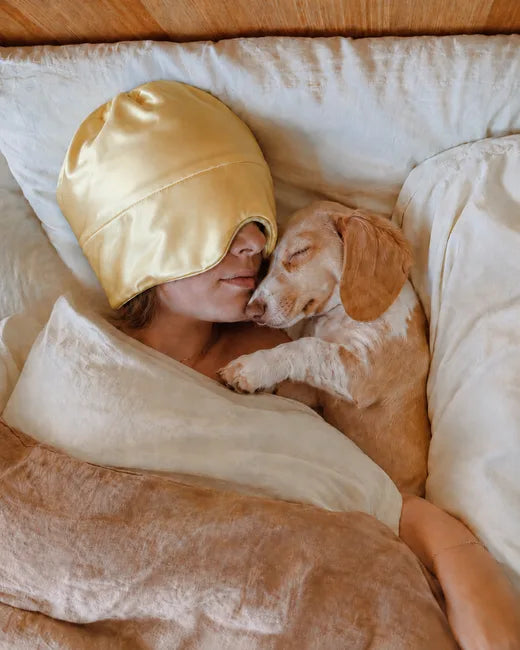 Customer wearing the yellow Sleep Hood in bed while cuddling her dog