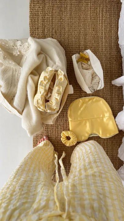 Yellow Sleep Hood and matching scrunchie laid out on a woven rug next to sleepwear